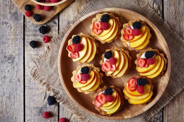 Fruit dessert tartlets with vanilla custard and fresh raspberries, blackberry, peach. Top view. Dark rustic style. — Stock Photo, Image