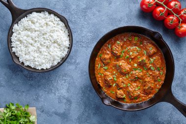 Madras tereyağı sığır baharatlı yavaş aşçı kuzu yiyecek pirinç ve dökme demir tavada domates ile