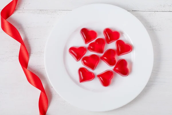 Heart shaped red jelly candies on white dish with ribbon on vint — Stock Photo, Image