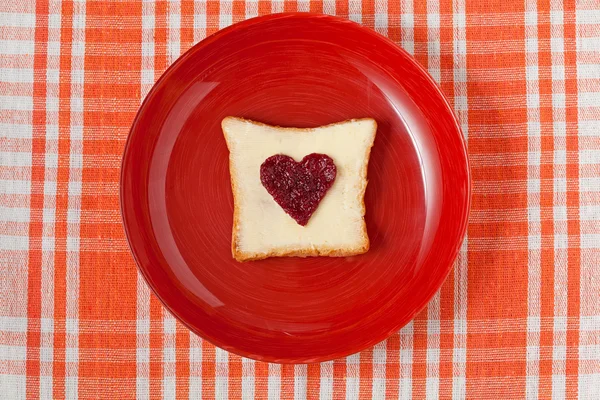 Здоровый тост из цельной пшеницы с джемом в форме сердца в красном блюде — стоковое фото