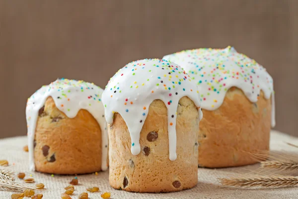 Baked sweet dessert traditional easter cake panettone also called kulich glazed with icing and raisins on vintage textile — Stock Photo, Image