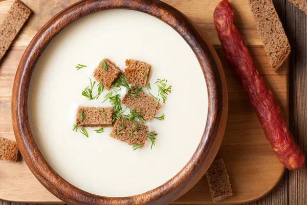 White cream soup with dill croutons and sausage in wooden bowl c — Stock Photo, Image