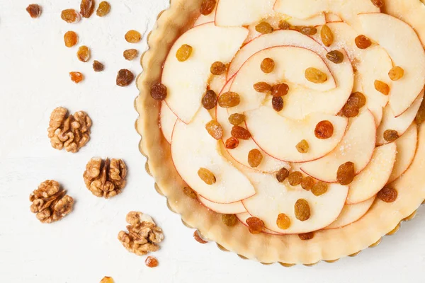 Tarta de manzana con pasas y preparación de nueces, Hornada casera cruda sobre mesa de cocina blanca —  Fotos de Stock