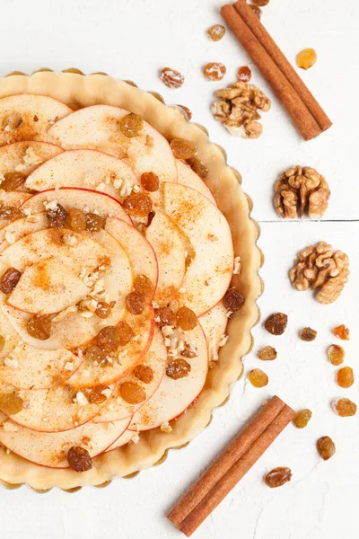 Homemade rustic apple pie preparation recipe. Tart with cinnamon, raisins and nuts on white table — Stock Photo, Image