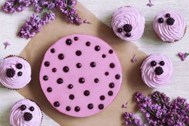 Traditional purple berry cupcakes and mousse dessert decorated with fresh berries on white kitchen table background. Top view. clipart