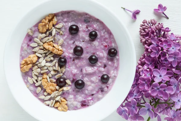 Healthy vegetarian diet meal. Clean eating oatmeal porridge with berries, nuts, and sunflower seeds in white plate. — Stock Photo, Image