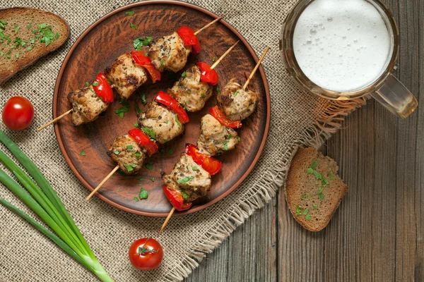 Delicious roasted turkey or chicken kebab skewers meat barbecue on clay dish with tomatoes and beer — Stock Photo, Image