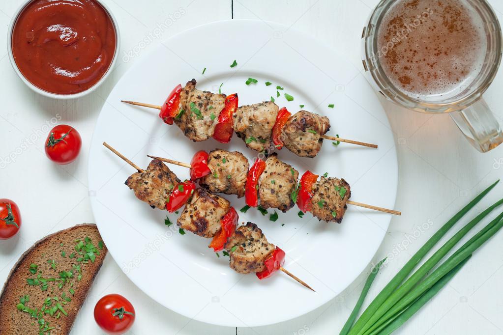 Delicious roasted turkey kebab skewer barbecue meat with vegetables, sauce and beer on white dish. Served kitchen table background.