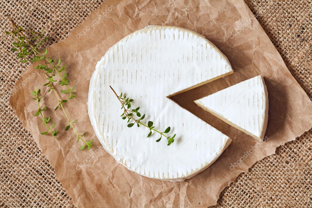 Sliced round camembert cheese traditional milk creamy dairy product with thyme on vintage parchment