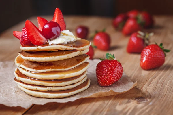 Homemade pancakes delicious breakfast or lunch dessert with strawberry, honey and butter on rustic kitchen table.