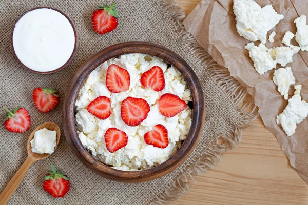 Healthy homemade cottage cheese breakfast or lunch with strawberry, sour cream and nuts in wooden dish on rustic kitchen table background — Stock Photo, Image