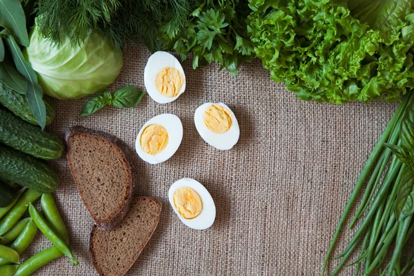 Πράσινα λαχανικά σύνθεση πλαίσιο με wholewheal ψωμί και τα αυγά σε ρουστίκ λινάτσα φόντο. μπιζέλια, λάχανο, αγγούρι, βασιλικό, άνηθο, κρεμμύδι, — Φωτογραφία Αρχείου