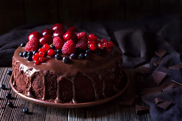 Традиційний домашній шоколадний торт солодкий десерт з коричневою глазур'ю, вишнями, малиною, смородиною на старовинному дерев'яному фоні . — стокове фото