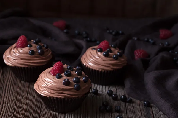 Cupcakes tradicionais caseiros de chocolate ou muffins sobremesa doce com creme de trigo, mirtilo e framboesa no fundo de madeira vintage Imagens Royalty-Free