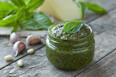 Homemade traditional mediterranean  healthy sauce in glass. Basil, parmesan, nuts and olive oil. Vintage wooden table background.