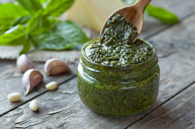 Traditional Italian pesto vegetarian food with basil nuts and olive oil. Wooden spoon gaining portion of sauce. Vintage wooden table background.
