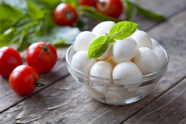 Traditional italian mozzarella cheese in glass bowl with basil and tomatoes caprese on rustic wooden background