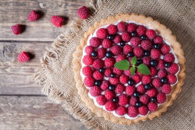 Gourmet homemade raspberry tart pie. Traditional cake with raspberries, blackberry and whipped cream on vintage wooden background