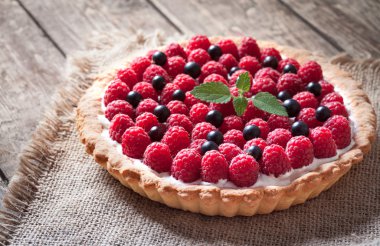 Delicious traditional homemade sweet raspberry tart cake dessert. Creamy pie with raspberries, whipped cream and mint on vintage rustic background.