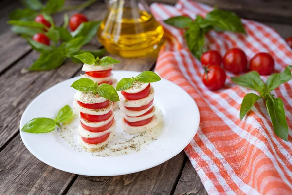 Traditional Italian caprese salad antipasti with sliced mozzarella tomatoes basil and olive oil on white dish. Vintage wooden table background — ストック写真