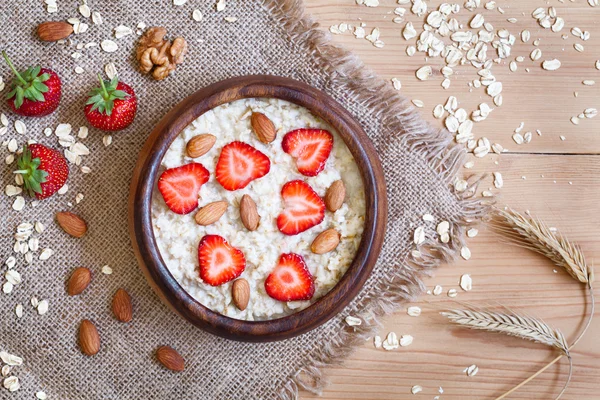 Healthy breakfast oatmeal porridge diet nutririon with strawberry and nuts. Organic vegetarian meal. Vintage wooden table background.