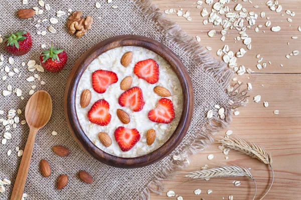 Healthy prepared oatmeal porridge breakfast with strawberries and nuts in wooden bowl on vintage table background — Stock Photo, Image