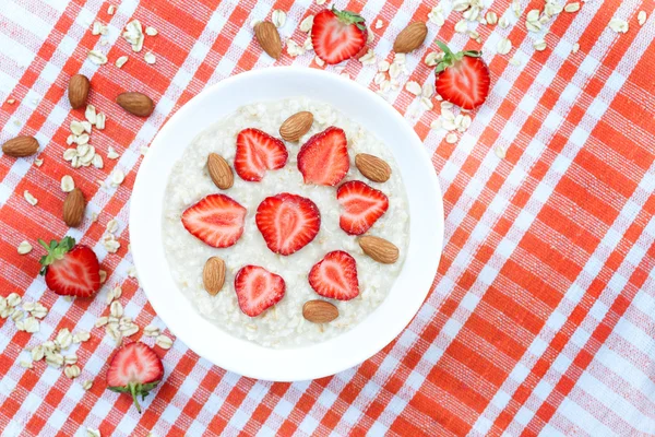 Healthy organic breakfast oatmeal porridge with strawberry and nuts in white bowl on vintage wooden table background — Stock Photo, Image
