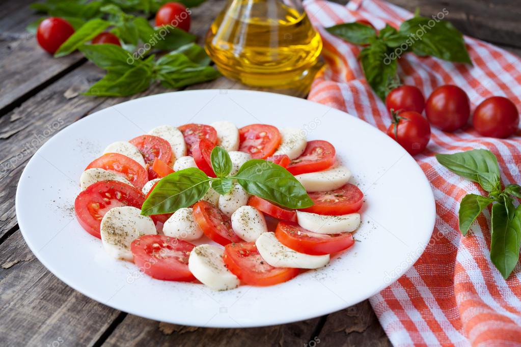 Healthy traditional Italian organic vegetarian caprese antipasti salad with sliced mozzarella tomatoes basil and olive oil on white plate. Vintage wooden table background