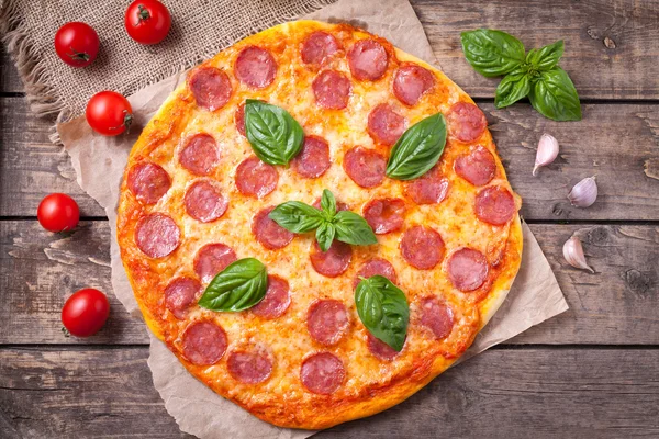 Traditionella pepperoni pizza italiensk läcker måltid med salami, mozzarellaost, tomater, basilika och vitlök på vintage träbord bakgrund — Stockfoto