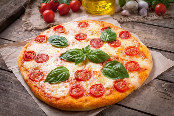 Tradiční domácí pečené italská pizza margherita s mozzarellou, bazalkou a rajčaty na pozadí historických dřevěný stůl. — Stock fotografie