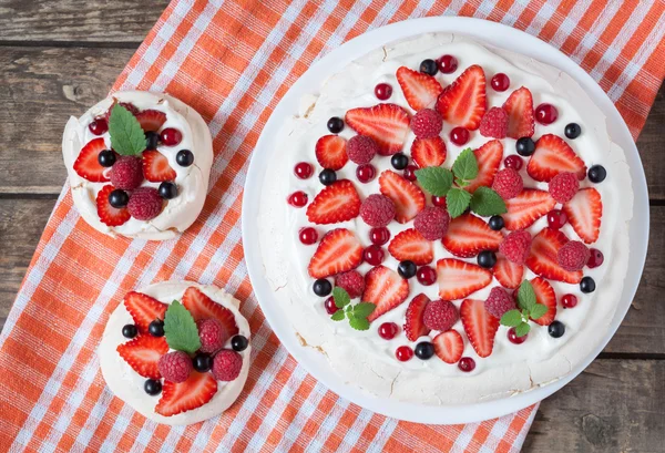 Gourmet homemade traditional Pavlova meringue sweet desset party cake with whipped cream, strawberry, blackberry and mint leaves on vintage wooden background. — Stock Photo, Image