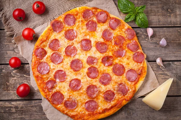 Domowe tradycyjne śródziemnomorskie pizza z pepperoni, ser mozzarella, pomidory, bazylia i czosnek na tle starodawny stół drewniany — Zdjęcie stockowe