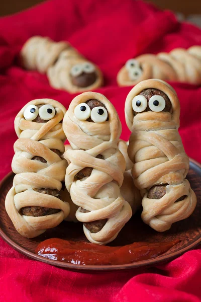 Funny meatballs sausage mummies in dough scary halloween celebration party food with eyes on red fabric background. — Stock Photo, Image