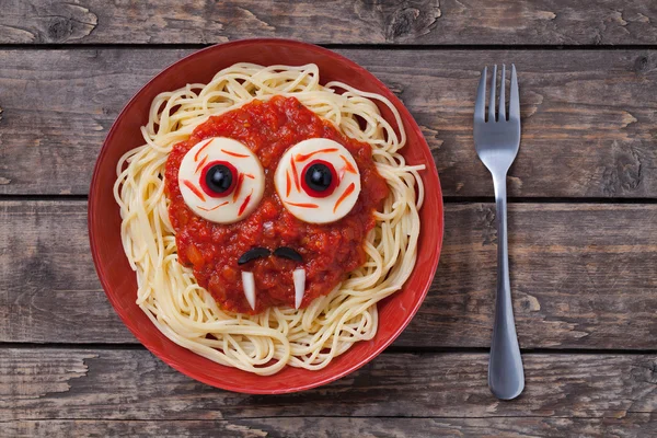 Halloween scary pasta food vampire face with big eyes and moustaches in red dish for celebration party decoration on vintage wooden table