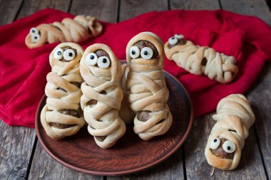 Scary halloween food meatball sausage mummies wrapped in dough with eyes  on vintage wooden background