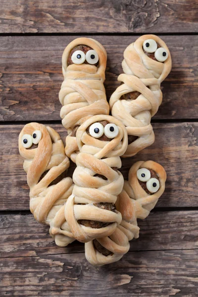 Scary halloween mummy sausages wrapped in dough with funny eyes for celebration party decoration. Vintage wooden background — Stock Photo, Image