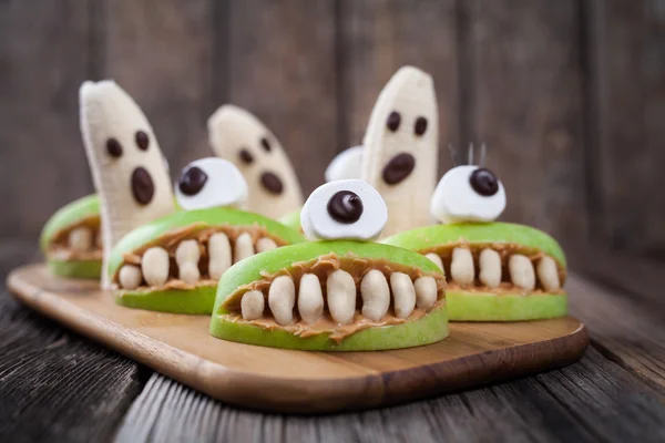 Halloween comestible miedo tratar boca cíclope manzana con dientes de mantequilla de maní y plátano fantasmas cara de chocolate. Receta saludable de postre vegetariano natural . — Foto de Stock