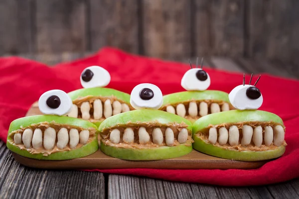 Cute scary halloween apple cyclop monsters food healthy vegetarian celebration party snack dessert recipe with red fabric on vintage wooden background — Stock Photo, Image