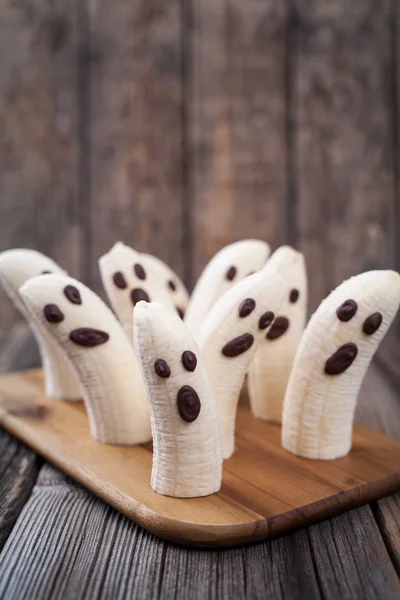 Scary Halloween plátano fantasma chocolate se enfrenta saludable receta de bocadillos naturales. Deliciosa decoración de fiesta sobre fondo de madera vintage . — Foto de Stock