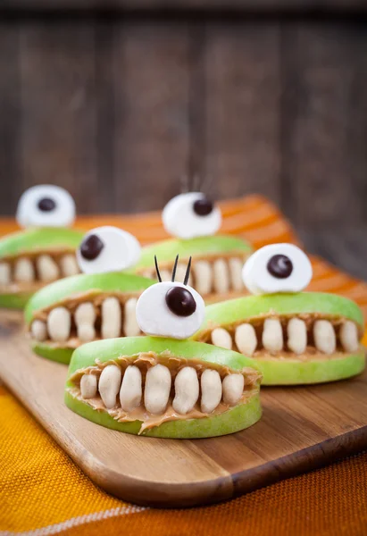 Scary halloween food monsters healthy natural snack sweets for party decoration recipe. Homemade spooky apple cyclops with teeth and peanut butter on vintage wooden table background. — Stock Photo, Image