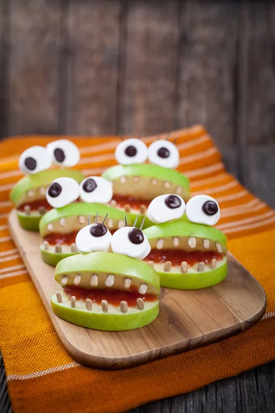 Homemade scary halloween edible monsters for celebration eve party decoration. Natural healthy sweets food recipe. Cute apples mouth with eyes, sunflower seeds and jam on vintage wooden background — Stock Photo, Image