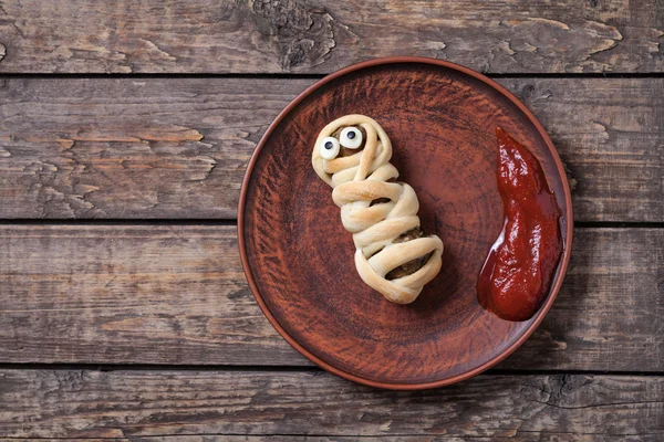 Funny halloween sausage mummy wrapped in dough celebration food on vintage wooden background. — Stock Photo, Image