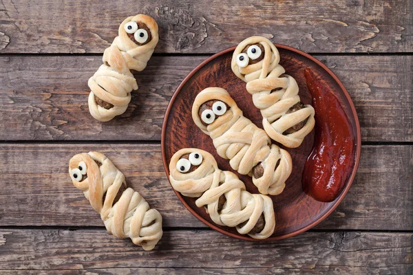 Funny sausage meatball mummies wrapped in dough scary halloween party decoration food on vintage wooden background — Stock Photo, Image