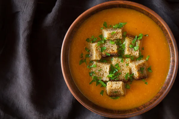 Healthy homemade pumpkin soup traditional recipe with croutons and chopped greens on dark cloth background — ストック写真