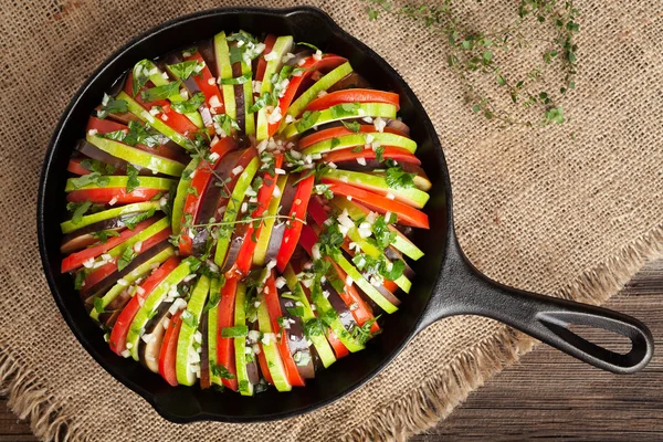 Traditional raw vegetable ratatouille in cast iron frying pan preparation recipe heathy organic vegetarian food on vintage wooden table background, top view. — Stock Fotó