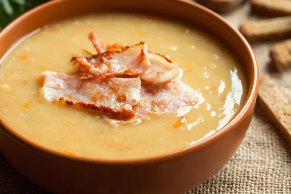 Split pea soup traditional german homemade recipe with pork bacon and croutons in clay dish on vintage wooden table background. — Stock Photo, Image