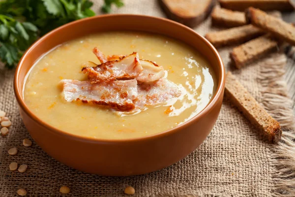 Pea soup traditional homemade german recipe in clay dish with greens and croutons on vintage wooden table background — Stock Fotó