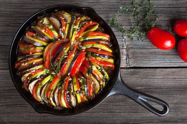 Vegetable ratatouille baked in cast iron frying pan traditional homemade healthy diet french vegetarian food on vintage wooden table background. Top view.