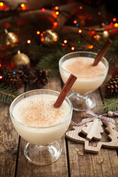 Eggnog christmas seasonal traditional non alcohol egg liqueur in two glass cups on vintage wooden table. Red bokeh background. — Stockfoto
