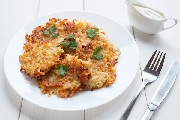 Potato pancakes or latke delicious homemade vegan food recipe with sour cream and greens on white wooden table background — Stock Photo, Image